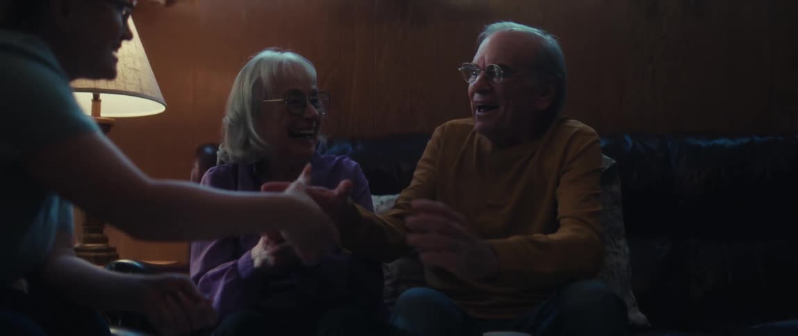 A young woman explains financial documents to an elderly couple, whose initial concern turns to joyful celebration and a loving embrace