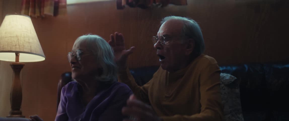 A financial advisor shares fantastic news with a senior couple, who celebrate with joyful laughter and a loving hug in their living room