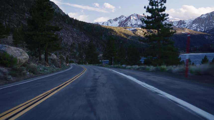 A point-of-view drive along a winding mountain road with majestic snow-capped peaks in the distance at sunrise