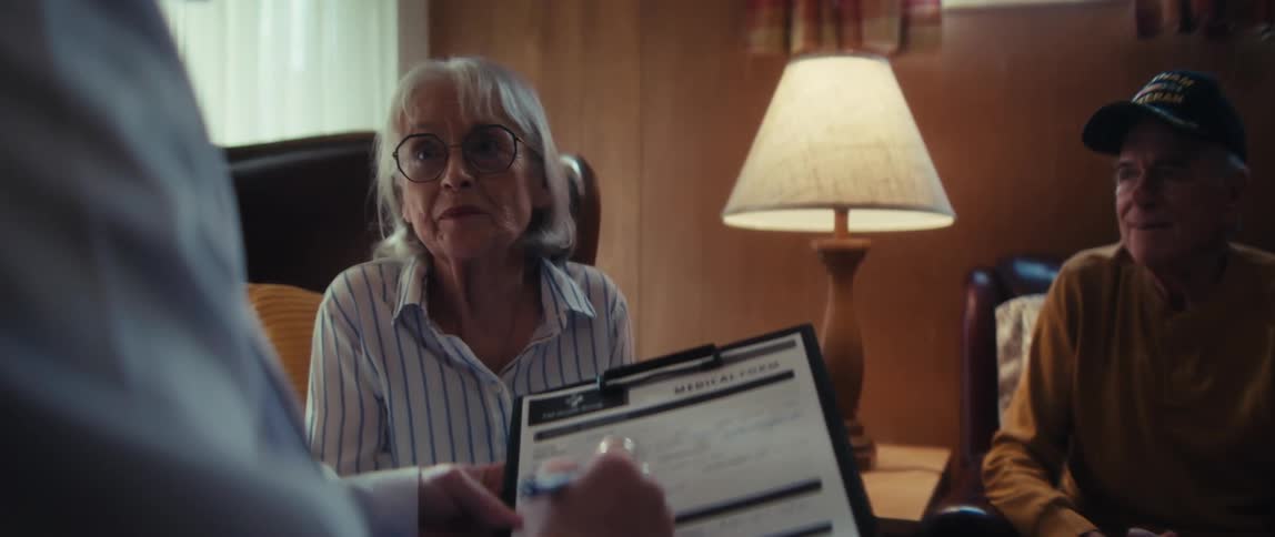 An elderly woman shares her medical history with a doctor who diligently fills out a patient form during a consultation