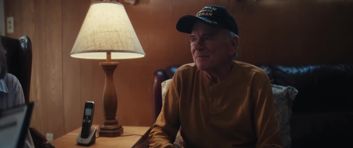 An elderly woman discusses a medical form with a healthcare professional while her husband, a Vietnam veteran, listens supportively