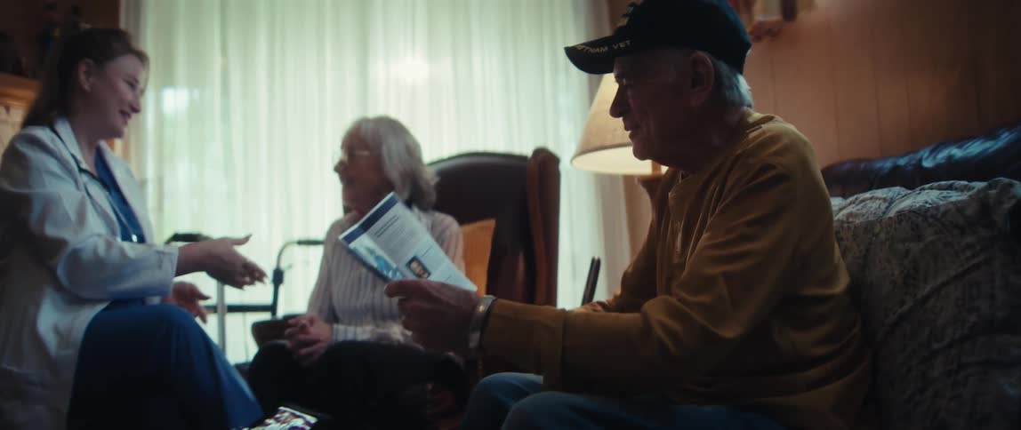 A caring female doctor on a house call gives a pamphlet to an elderly veteran and his wife in their living room