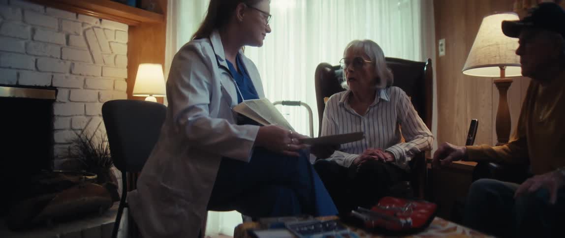 A compassionate doctor delivers difficult news to a senior couple, showing them a brain scan and offering comfort in their home