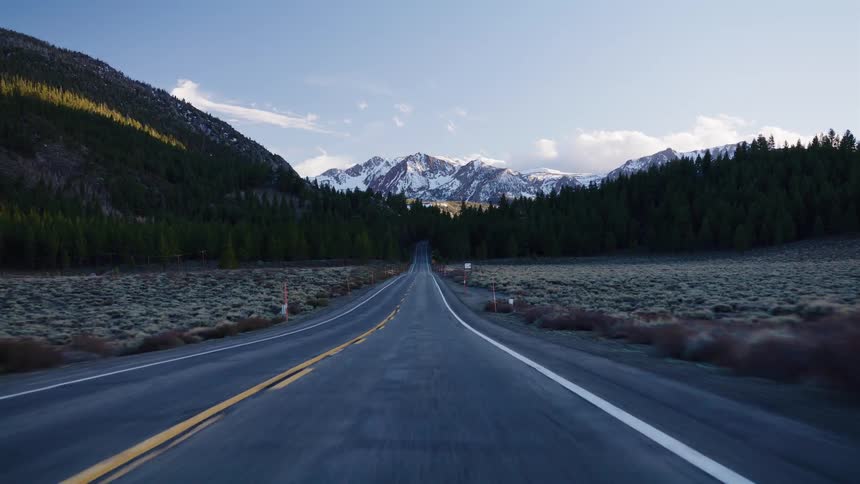 A point-of-view shot of driving down a scenic highway through a valley toward snow-capped mountains at sunrise
