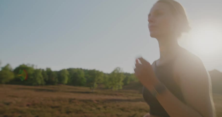 A determined woman jogs in slow motion through a beautiful sunlit heathland during golden hour