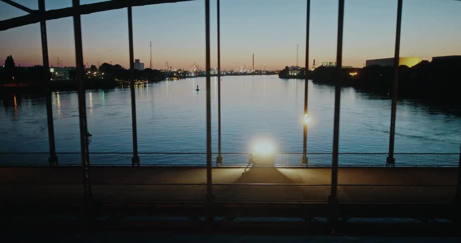 A runner jogs across a bridge in an industrial city with a river view during sunset