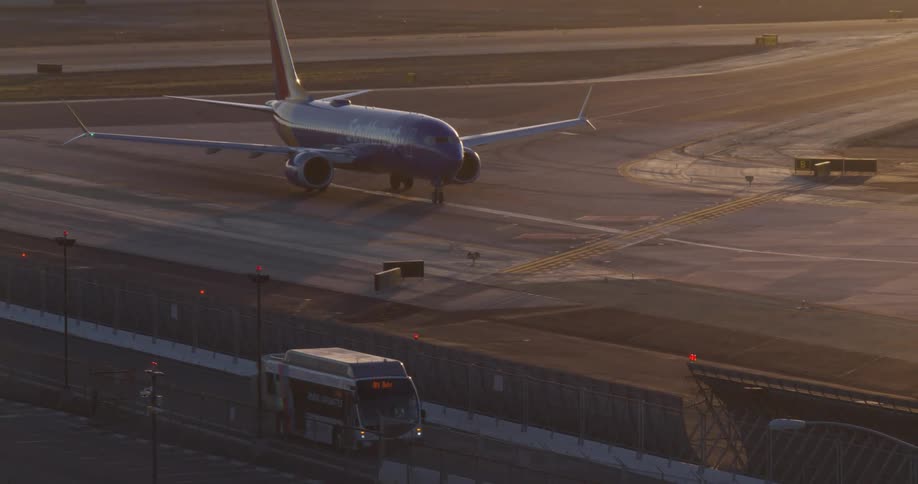 A Southwest Airlines airplane waits on the airport tarmac at golden hour as a shuttle bus drives past