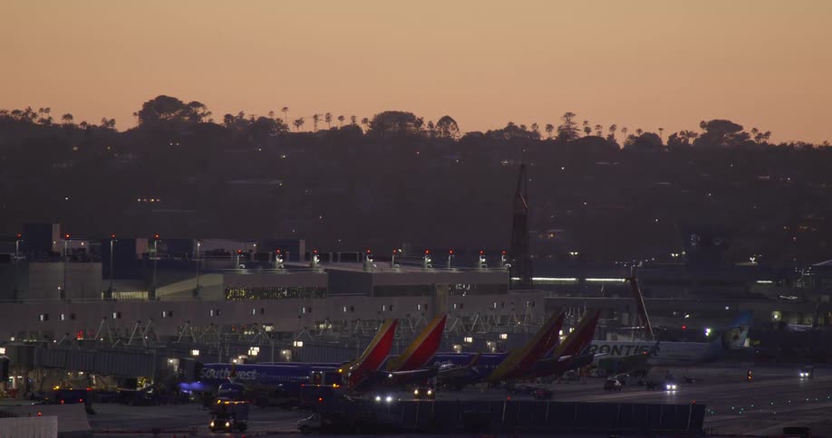 A wide view of a busy airport terminal at dusk, with airplanes at the gates and ground crew activity on the tarmac