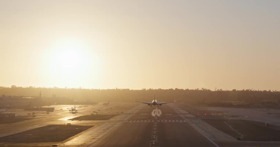 An airliner approaches and lands on a runway in slow motion with the golden light of the setting sun in the background