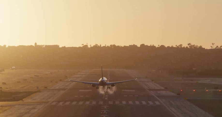 A passenger jet is seen from behind as it comes in for a landing on an airport runway during a hazy golden sunset