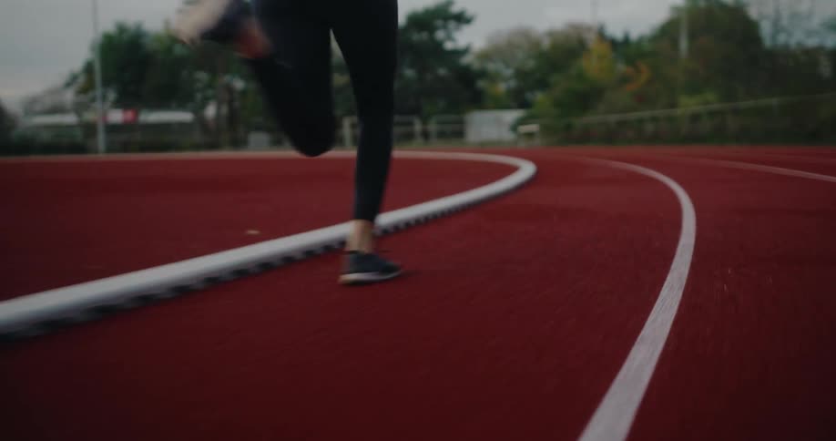 A female runner's legs in slow motion as she sprints along a red athletic track