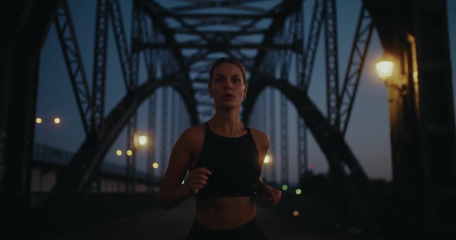 An athletic woman maintains a steady pace as she jogs along a large industrial bridge during her early morning workout