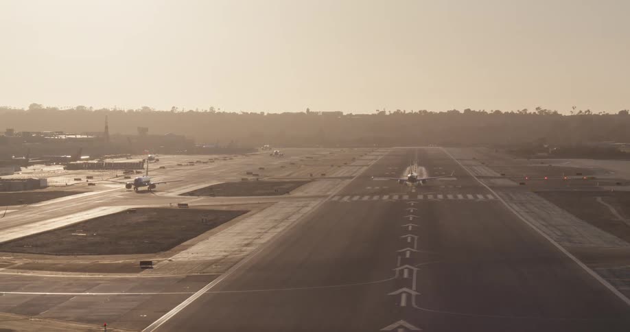 A passenger jet accelerates down an airport runway and takes to the skies during a hazy golden hour