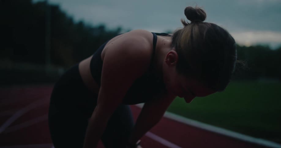 Exhausted female athlete catching her breath on a running track after a workout at dusk