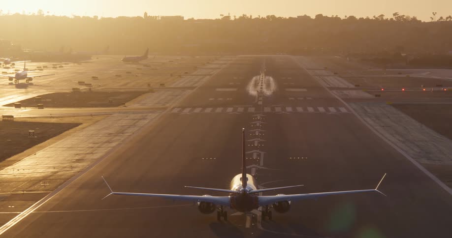 A passenger airplane taxis down the runway, preparing for takeoff into the hazy golden sunset