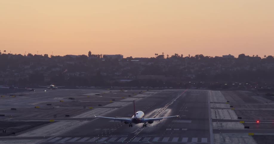 Slow-motion telephoto view of a commercial airliner landing on a runway as the sun sets, with wheels smoking upon contact with the tarmac