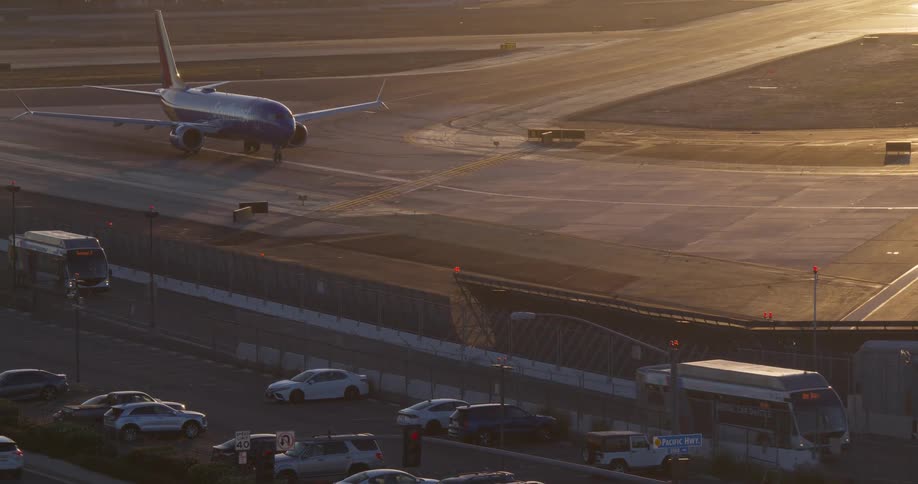 An airliner taxis on the tarmac at golden hour as airport traffic moves in the foreground