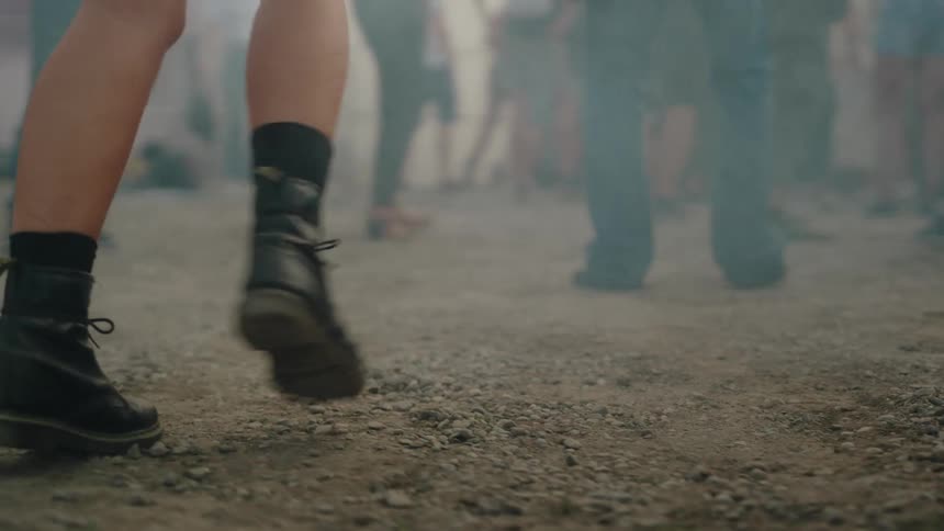 Low angle slow motion shot of people's feet dancing on a gravel ground at an outdoor festival with smoke effects