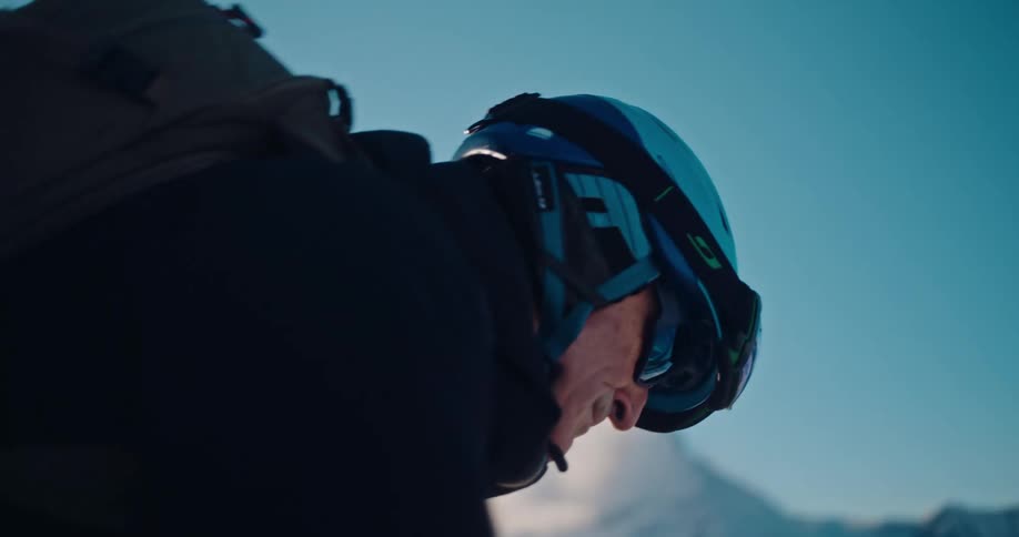 A skier carefully attaches climbing skins to his skis in slow motion on a sunny, snowy mountain