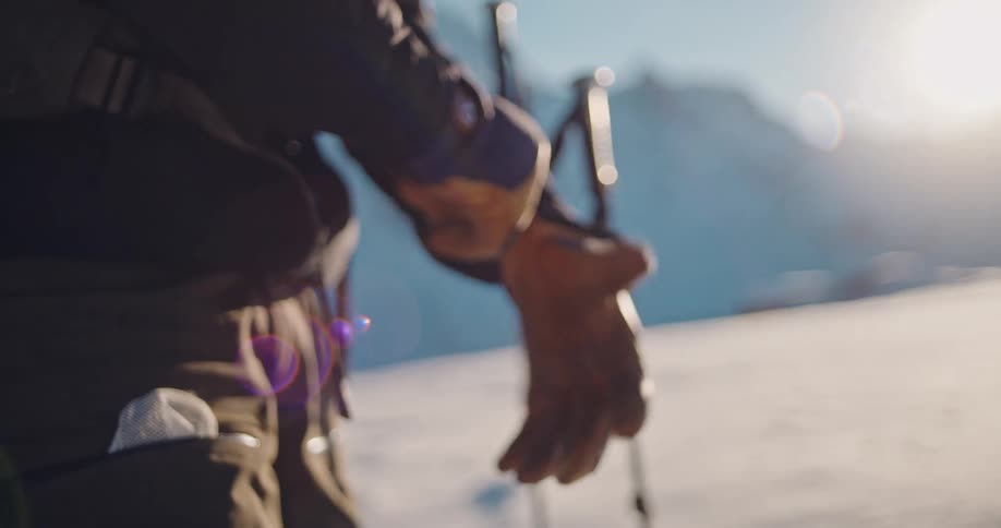 A close-up slow-motion shot shows a skier putting on his warm gloves on a sunny winter day in the mountains