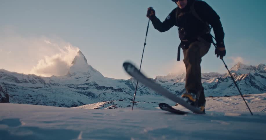A male skier enjoys an epic ski tour through the snowy Alps in slow motion, with the iconic Matterhorn mountain in the distance