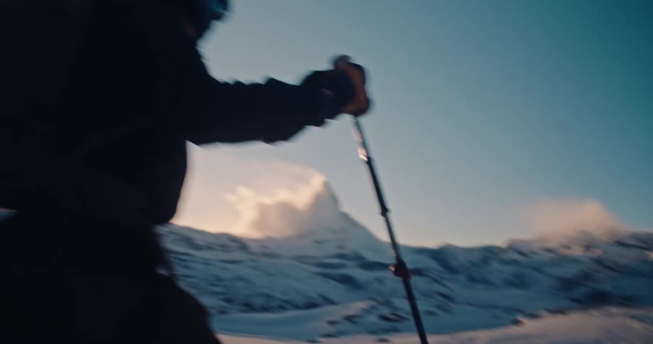 A determined mountaineer hikes through a vast snowy landscape in the Swiss Alps with the Matterhorn in the background at sunrise