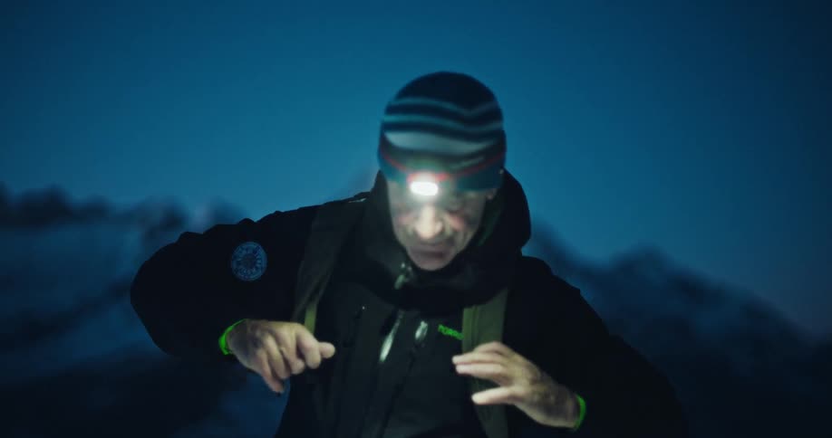 A mountaineer uses a ferro rod to create sparks for a fire in the cold mountains at night, illuminated by his headlamp