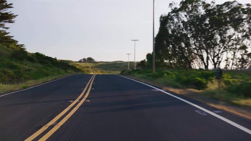 A smooth point-of-view drive on a winding country road through rolling green hills at golden hour