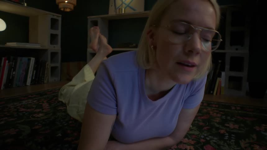 A young woman wearing glasses studies late at night, lying on the floor with her laptop and textbooks