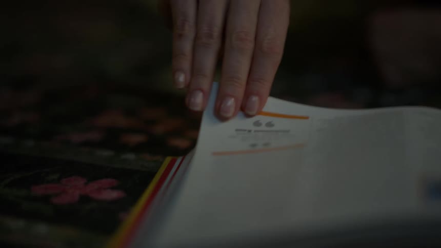 A close-up shot shows a hand slowly following the text in a book before turning the page