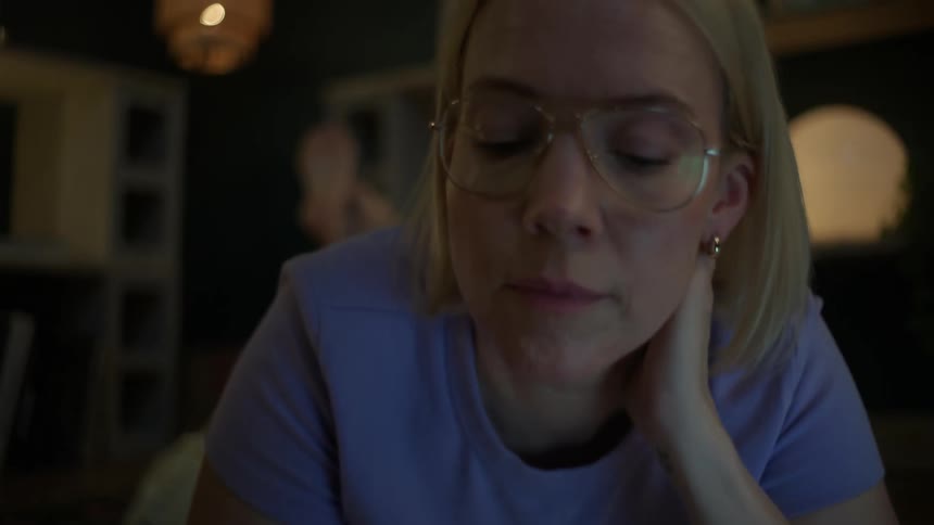 Close-up rack focus from a textbook to a focused woman with glasses studying on the floor at night