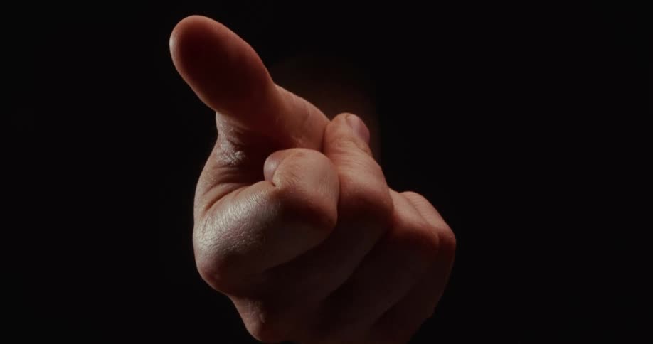 A dramatically lit hand slowly beckons with its index finger against a solid black background