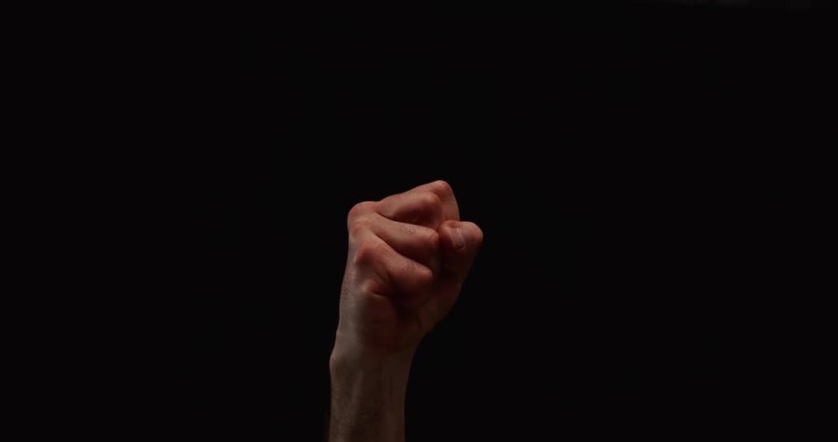 A male hand dramatically closes into a tight fist in slow motion against a black background