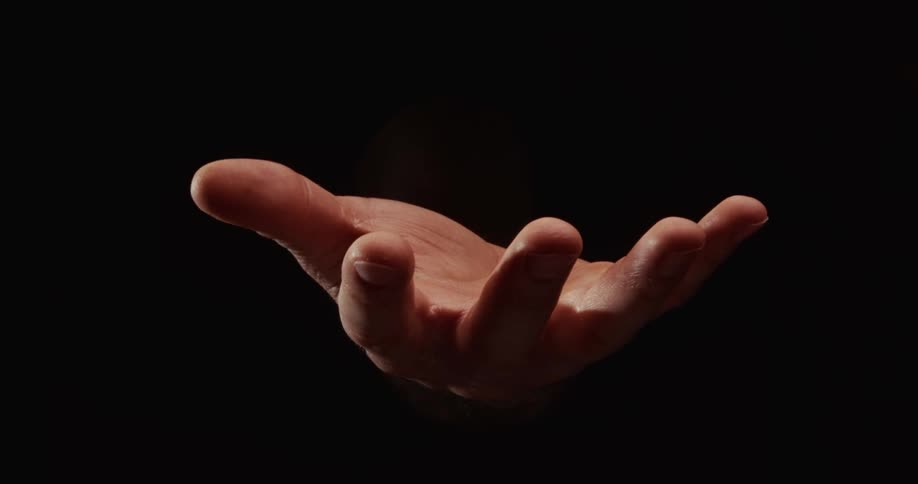 A dramatic close up of a cupped hand emerging from darkness into light and then retreating