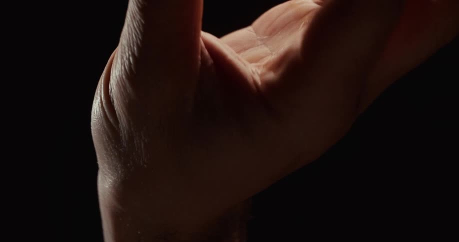 Dramatic slow-motion close-up of a hand clenching into a fist and slowly opening into a palm against a black background