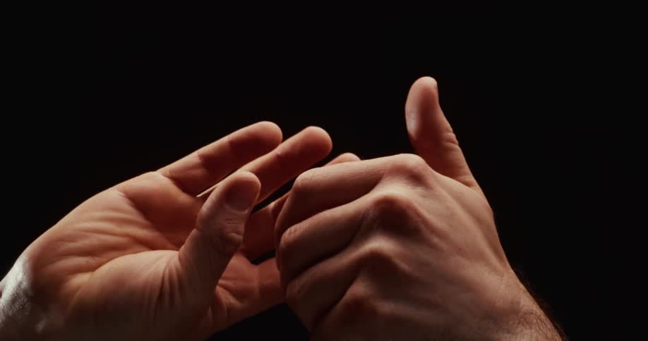 A dramatic closeup shows a pair of hands moving slowly and deliberately, fingers gently interlacing against a stark black background