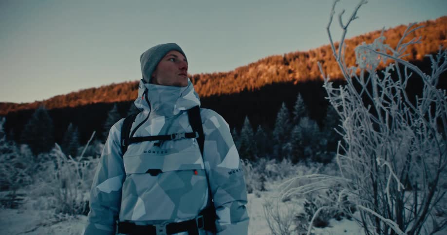 A man in a winter jacket admires a beautiful, frosty mountain landscape during a golden sunrise