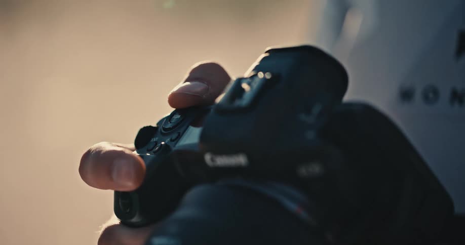 Close-up of a photographer's hands adjusting the dials and buttons on a DSLR camera in warm, golden hour light