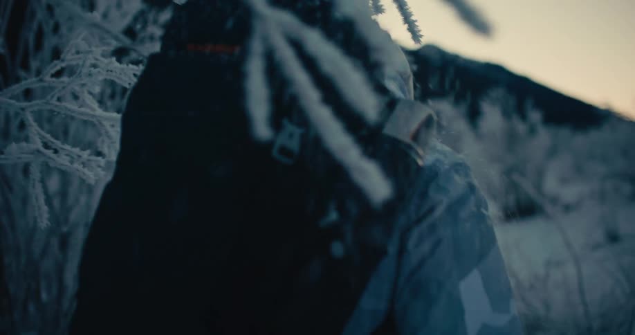Over-the-shoulder slow motion shot of an adventurer hiking through a frozen, snowy landscape at sunrise