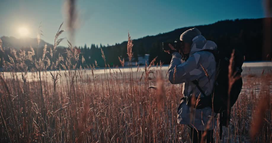 An adventurous female photographer captures the stunning winter landscape while standing in a field of golden reeds at sunrise
