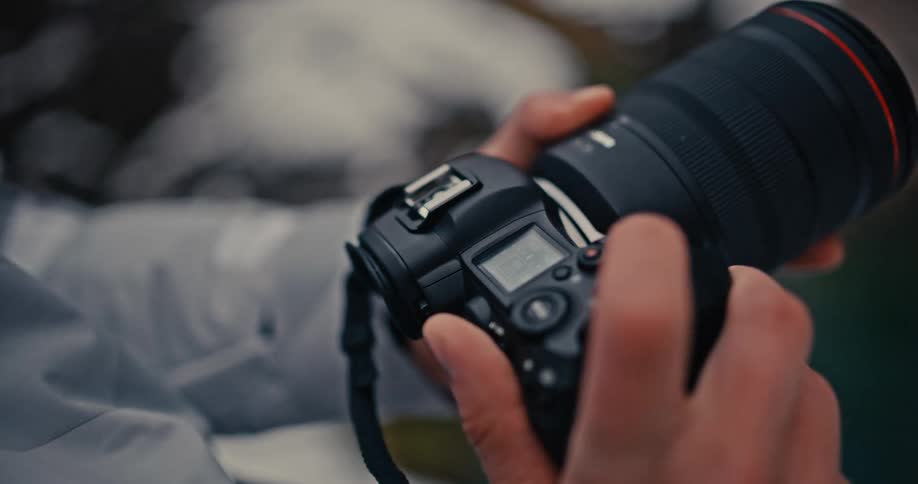 A close-up shot of a photographer's hands adjusting the settings on a professional digital camera outdoors