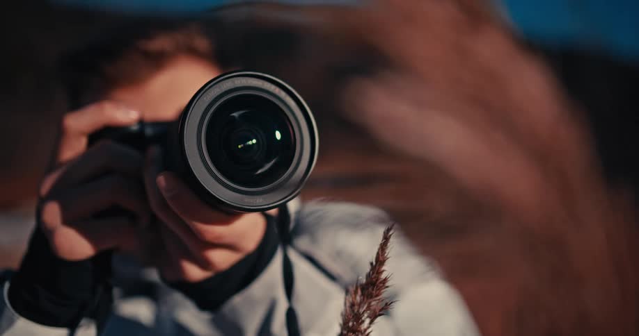 Close-up shot of a male photographer pointing a camera at the viewer and adjusting the lens focus in a sunlit field