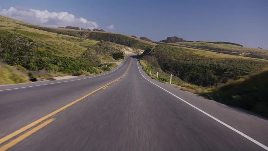 A scenic point-of-view drive along a winding two-lane road through rolling green hills on a sunny day