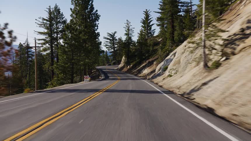 A point-of-view shot while driving along a winding mountain road surrounded by tall pine trees and rocky cliffs on a sunny day