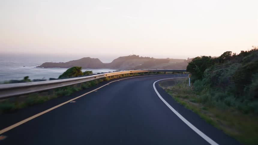 A smooth, scenic drive along a winding coastal highway reveals the ocean and a beautiful sunrise