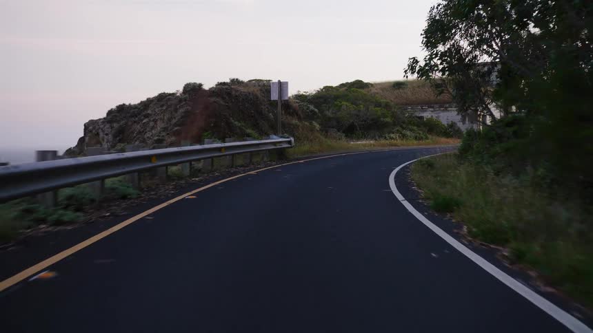 A slow drive along a winding coastal road at dusk reveals old, abandoned military bunkers built into the hillside