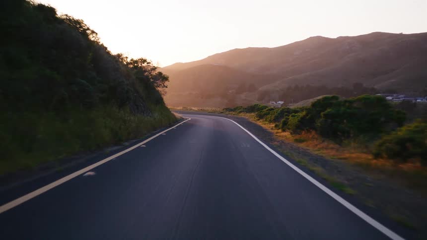 A scenic point-of-view drive on a winding coastal mountain road as the golden sun sets over the hills