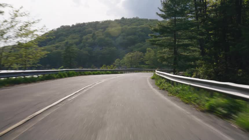 A POV drive on a winding road through a sunlit forest alongside a river