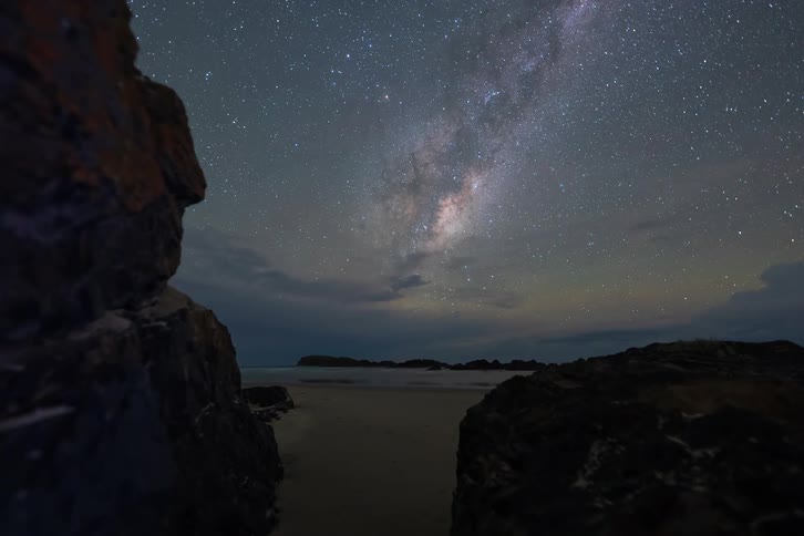 Stunning night sky timelapse of the Milky Way with a distant thunderstorm over a rocky beach