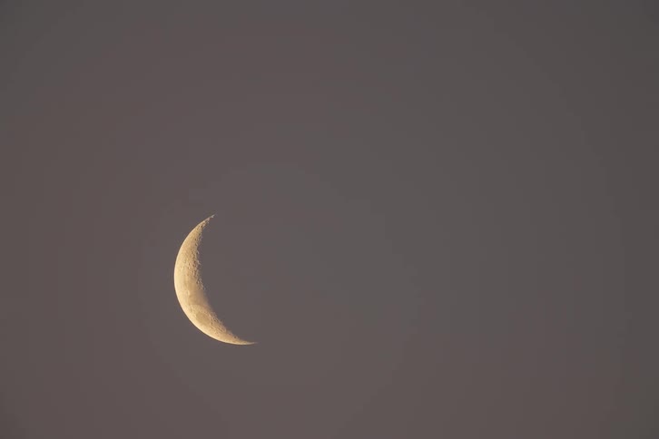 Serene time-lapse shows a detailed crescent moon arcing across the dusky sky